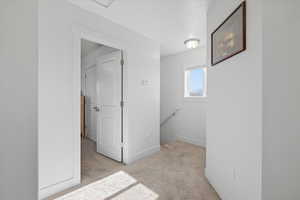 Hallway with an upstairs landing with a window, and light carpet