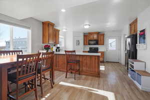 Kitchen featuring wood finish cabinets, a peninsula, granite countertops, light wood finished floors, and black appliances