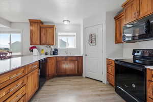 Kitchen featuring black appliances, wood finish cabinetry, light wood-style flooring, and light stone countertops