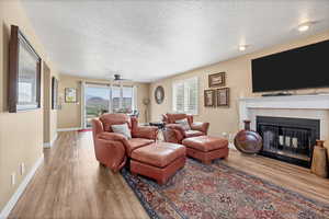 Living area featuring a textured ceiling, light wood finished floors, a fireplace, and ceiling fan