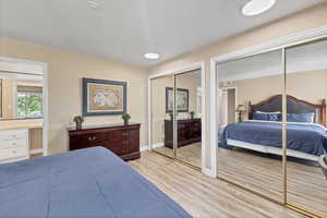 Bedroom with multiple closets, light wood-style flooring, and a textured ceiling
