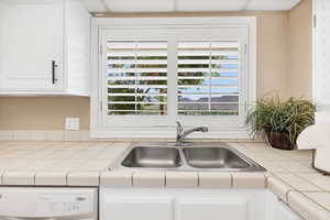 Kitchen view of tile counters, white cabinetry, and dishwasher