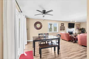 Dining room featuring a glass covered fireplace, light wood-style flooring, and ceiling fan