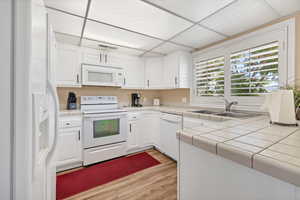 Kitchen featuring white appliances, white cabinets, a paneled ceiling, tile counters, and light wood finished floors