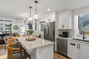 Kitchen featuring open floor plan, white cabinetry, stainless steel appliances, light stone counters, and light wood-style floors