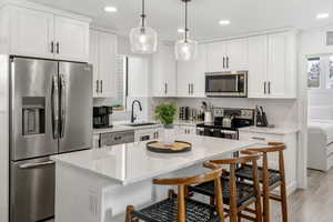 Kitchen with stainless steel appliances, white cabinets, light stone countertops, and a breakfast bar