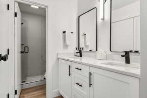 Bathroom featuring a shower stall, double vanity, and light wood-style flooring
