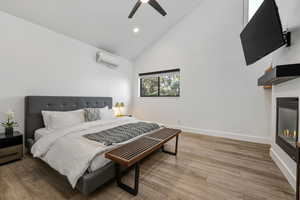 Bedroom with light wood-style flooring, vaulted ceiling, a glass covered fireplace, ceiling fan, and recessed lighting