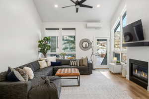 Living area with wood finished floors, a glass covered fireplace, vaulted ceiling, ceiling fan, and recessed lighting