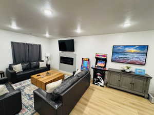 Living area featuring light wood-style flooring, a glass covered fireplace, and a textured ceiling