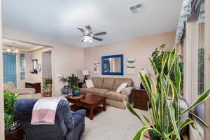 Living area featuring a ceiling fan, suspended lighting, and carpet