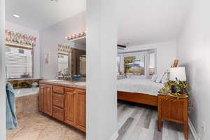 Primary bedroom with ensuite full bath, double vanity, a bath, and light wood finished floors