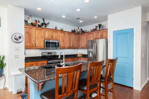 Kitchen featuring a breakfast bar area, granite countertops, wood finish cabinets, stainless steel appliances, and engineered wood flooring