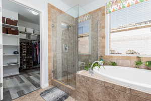 Primary bathroom featuring a spacious closet, a bath, a stall shower, and travertine tile floors