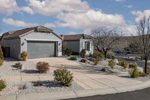 View of front facade featuring driveway, a garage, stucco siding, a tile roof, and stone siding