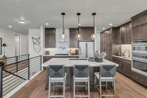 Kitchen with dark wood finish cabinets, hanging light fixtures, a breakfast bar, stainless steel appliances, and an island with sink