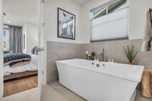 Full bathroom featuring tile walls, ensuite bath, light tile patterned floors, a freestanding tub, and a wainscoted wall