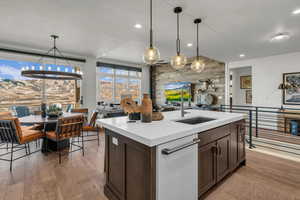 Kitchen featuring dark wood finish cabinets, light wood-type flooring, decorative light fixtures, open floor plan, and an island with sink
