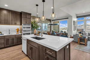 Kitchen featuring dark wood finish cabinetry, open floor plan, light wood-style floors, hanging light fixtures, and light stone counters