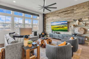 Living room with wood walls, a wood stove, wood finished floors, and ceiling fan