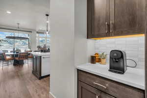 Kitchen featuring dark wood finish cabinetry, decorative backsplash, light wood finished floors, decorative light fixtures, and light stone counters