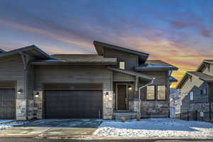 View of front of property featuring stone siding, concrete driveway, an attached garage, and a shingled roof