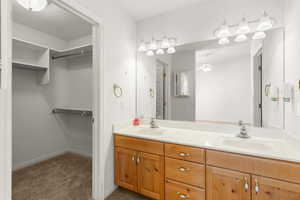 Full bath with double vanity, a spacious closet, light carpet, and a ceiling fan