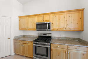 Kitchen with stainless steel appliances, light wood finish cabinets, light stone counters, and light tile patterned floors