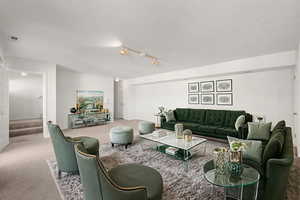 Carpeted living area featuring stairs and rail lighting