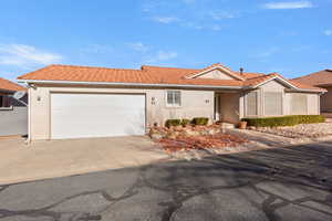 Ranch-style house featuring a tiled roof, stucco siding, concrete driveway, and an attached garage