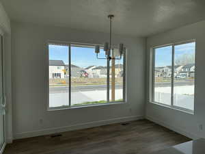 Unfurnished dining area featuring a textured ceiling, a chandelier, dark wood-type flooring, and a residential view