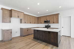 Kitchen with tasteful backsplash, stainless steel appliances, a center island with sink, light wood-style floors, and recessed lighting