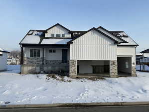 View of front of home with stone siding, covered porch, a garage, and board and batten siding