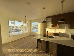 Kitchen with decorative light fixtures, light stone counters, dark brown cabinets, a chandelier, and a textured ceiling
