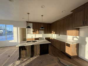 Kitchen with dark brown cabinets, dark wood-type flooring, an island with sink, pendant lighting, and a textured ceiling