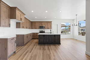 Kitchen with a chandelier, light stone countertops, tasteful backsplash, light wood-style flooring, and an island with sink