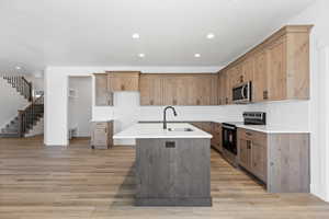 Kitchen featuring stainless steel appliances, decorative backsplash, a center island with sink, light wood-style floors, and light stone countertops