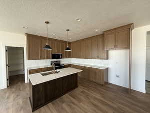 Kitchen featuring decorative backsplash, light stone counters, an island with sink, stainless steel appliances, and a textured ceiling