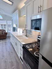 Kitchen with a textured ceiling, stainless steel appliances, vaulted ceiling, light countertops, and white cabinets