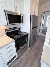 Kitchen with stainless steel appliances, light countertops, white cabinets, dark wood finished floors, and vaulted ceiling