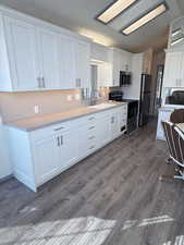 Kitchen featuring white cabinetry, stainless steel appliances, light countertops, dark wood finished floors, and vaulted ceiling