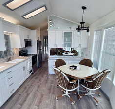 Kitchen featuring white cabinetry, stainless steel appliances, hanging light fixtures, light wood-style floors, and lofted ceiling