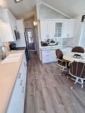 Kitchen featuring white cabinets, lofted ceiling, appliances with stainless steel finishes, light countertops, and light wood finished floors
