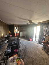 Carpeted living area featuring wooden walls, ceiling fan, washer and clothes dryer, and a textured ceiling