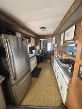 Kitchen with light floors, freestanding refrigerator, white cabinetry, dark countertops, and black dishwasher