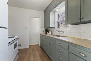 Kitchen featuring light stone countertops, white appliances, dark wood finished floors, green cabinets, and backsplash