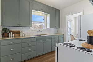 Kitchen featuring white appliances, dark wood-type flooring, tasteful backsplash, light stone countertops, and green cabinetry