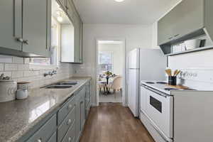 Kitchen featuring white appliances, dark wood-type flooring, a textured ceiling, light stone counters, and backsplash