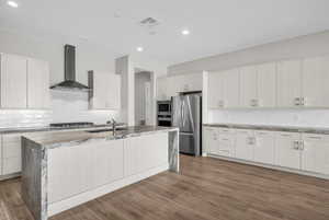 Kitchen featuring light stone counters, backsplash, stainless steel appliances, a center island with sink, and light wood finished floors