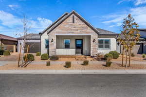 View of front of property with stone siding, a porch, driveway, an attached garage, and stucco siding